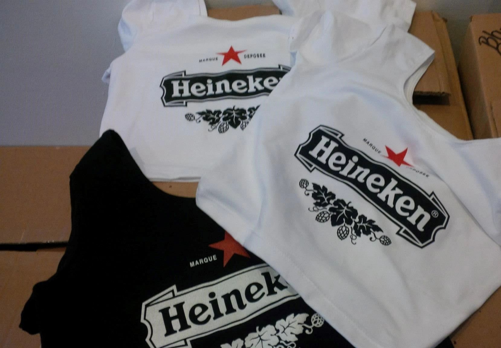 White and black tees display Heineken branding, showing the same identity across contrasting garment colors.