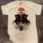A white tee features a dark illustrated design beneath a warm-colored circular accent. Only the original small thumbnail has been recovered.