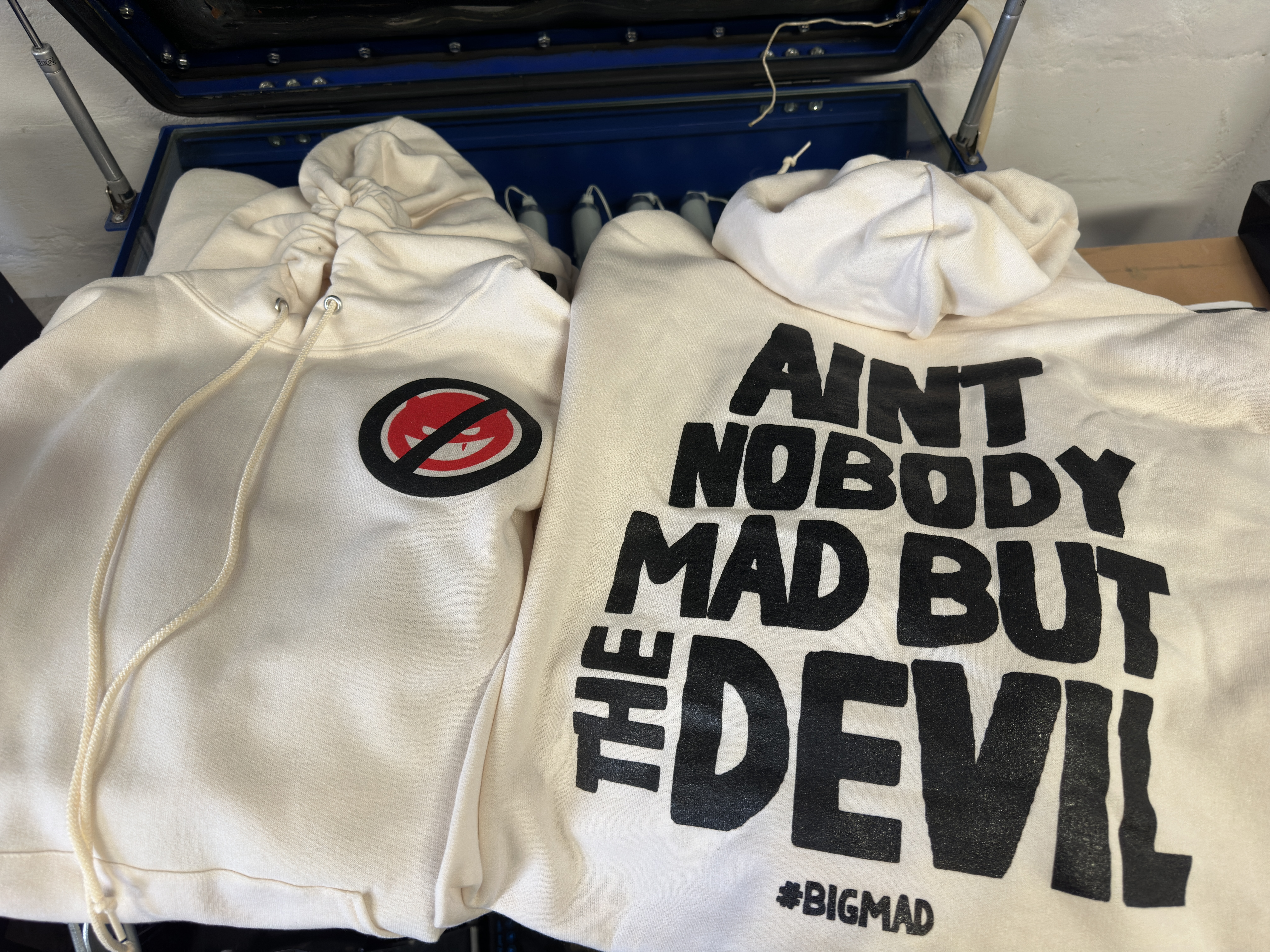 Light hoodies combine bold black lettering with a red-and-black circular graphic. The large type reads “Ain’t Nobody Mad But the Devil.”