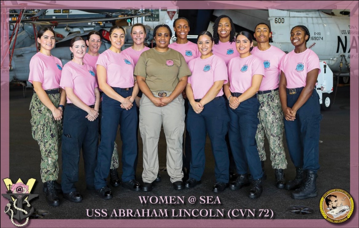 A group photograph labeled Women at Sea and USS Abraham Lincoln (CVN 72). Pink shirts appear alongside uniforms; this image is preserved as it appeared in the original gallery.