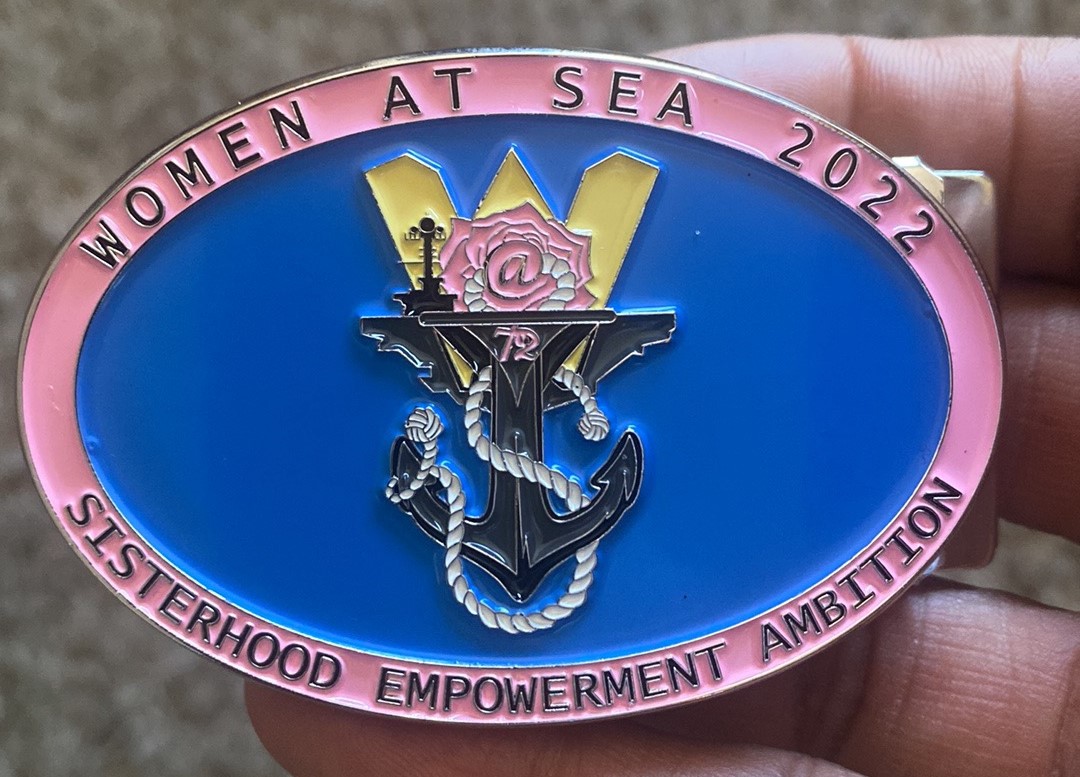 A close view of the Women at Sea crest: an anchor, star and circular lettering in pink, blue and gold, with the words “Sisterhood • Empowerment • Ambition.”